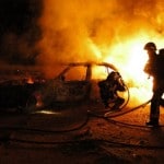 une voiture brule à coté de pompiers tentant d'éteindre le feu. delinquance nouvel an