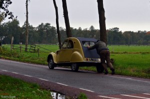 une homme entrain de pousser une 2cv citroen