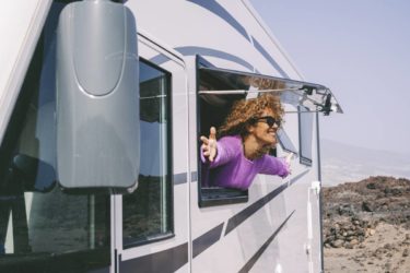 Une personne souriante et épanouie à l'intérieur d'un camping-car, profitant d'un moment de détente en voyage