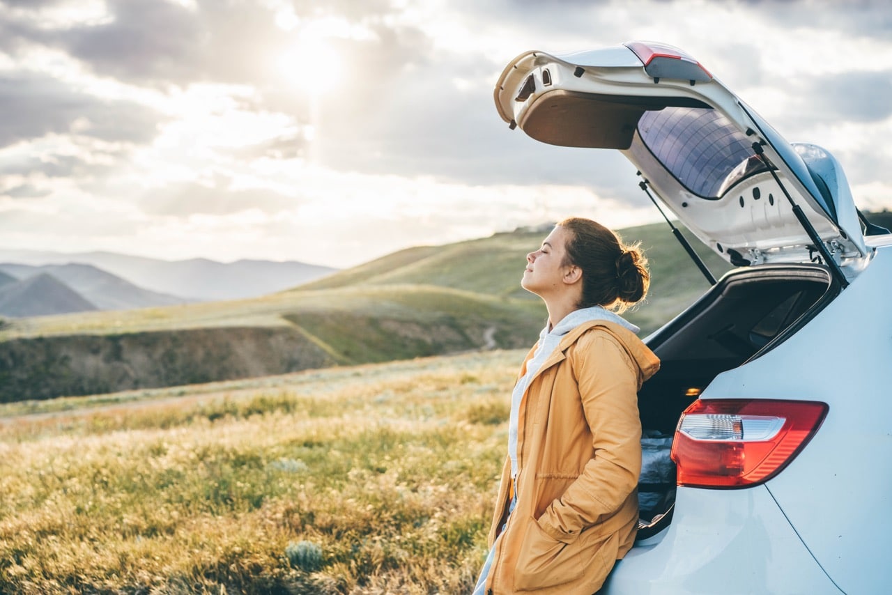 Une jeune femme en vacance avec sa voiture de location qui lui permet de se déplacer où elle veut