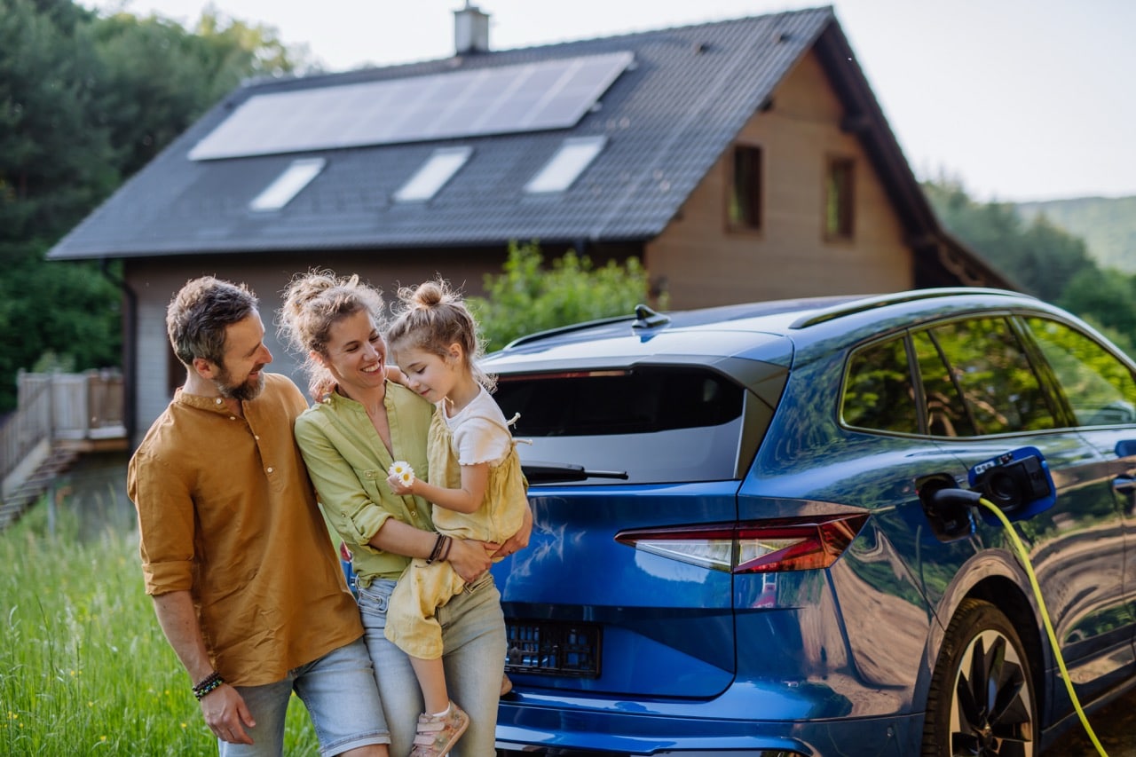 Famille souriante devant une voiture électrique en recharge, illustrant un mode de vie écologique et durable à la campagne
